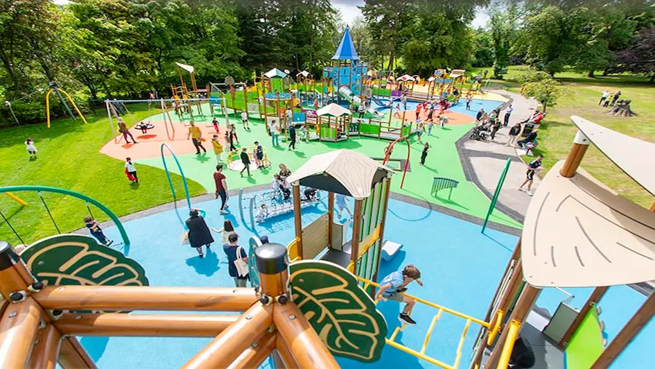 A vibrant playground filled with children happily playing on swings, slides, and climbing structures under a sunny sky.