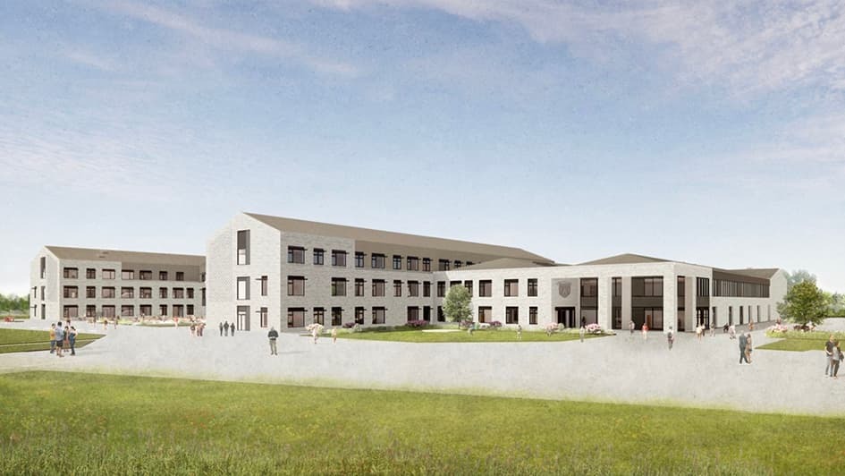 A modern, three-story, L-shaped building with large windows and a light facade stands under a blue sky, surrounded by green grass and scattered people.