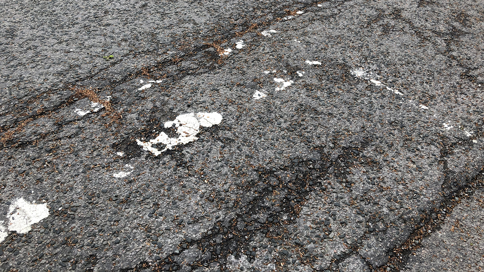 Cracked asphalt road with faded white paint lines and scattered debris, conveying a sense of wear and age, suggesting frequent use over time.